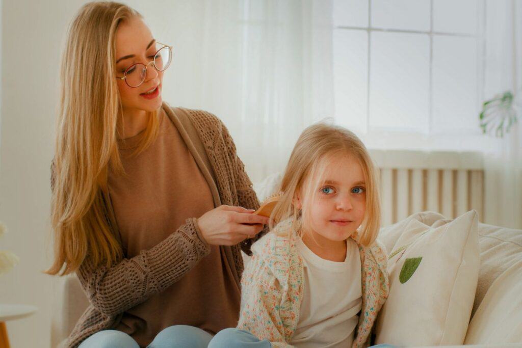 Young blonde mom fixing her young daughter's hair.