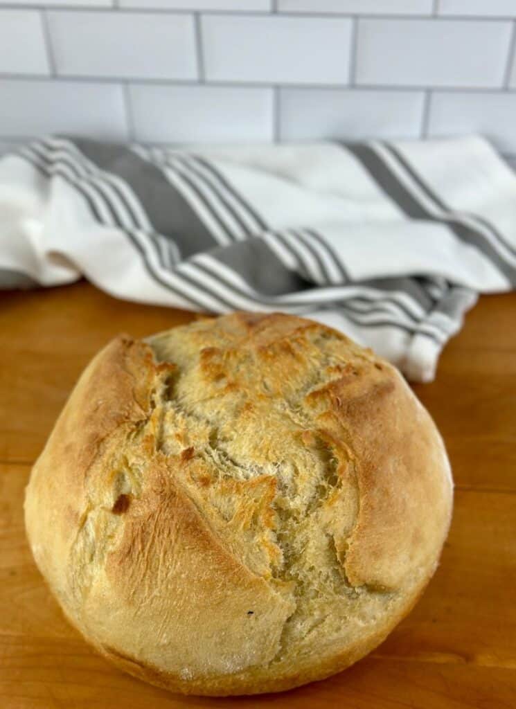 Vertical image of finished loaf of dutch oven bread on a wooden counter.