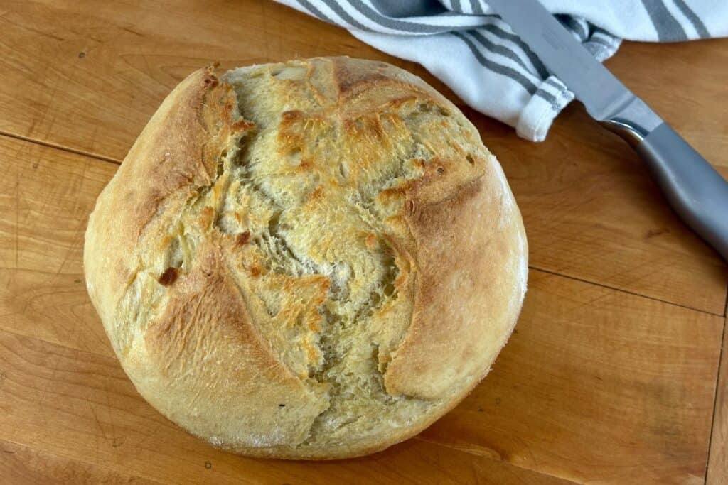 Crusty french artisan loaf on wooden table with serrated knife.