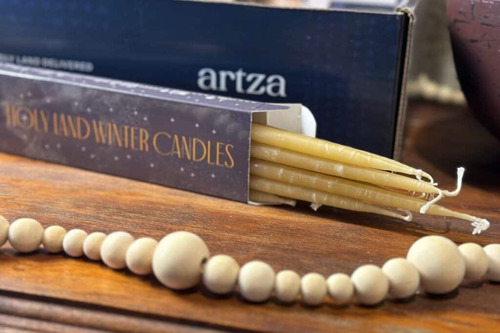 Beeswax candles peeping out of their box on a decorated tabletop- included in this year's Artza Christmas box.