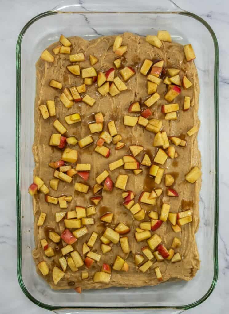 Apple butter blondie batter in a 9x13 glass baking dish with cinnamon coated apples scattered over the top.