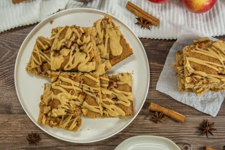 Apple butter blondies with maple glaze on a wooden table with cinnamon sticks and star anise decorating the table nearby.