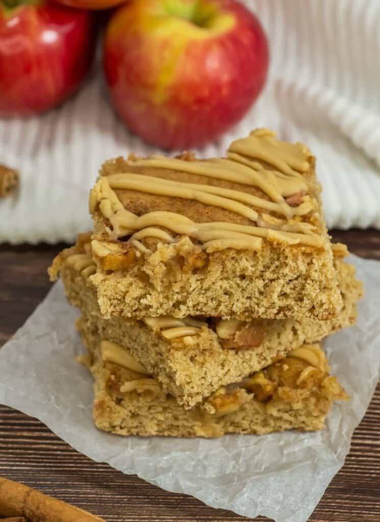 3 apple butter blondie bars in a stack on parchment paper with fresh apples in background.