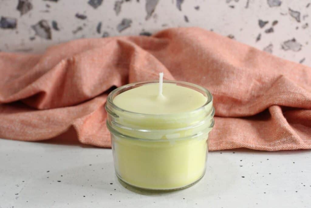 Beeswax candle in a small glass jar on speckled countertop.