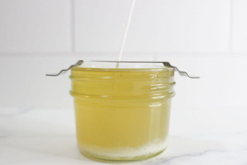 Candle sitting on counter while wax is hardening, with wick holder in place.