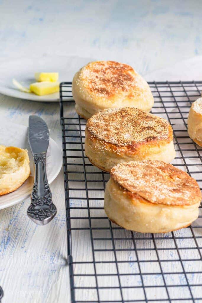 Sourdough English muffins in a row on a cooling rack.