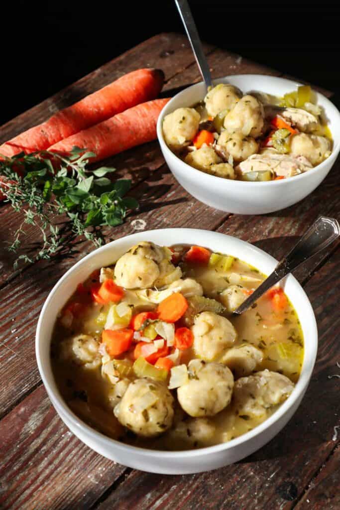 Two bowls of chicken, vegetables and dumplings in broth.