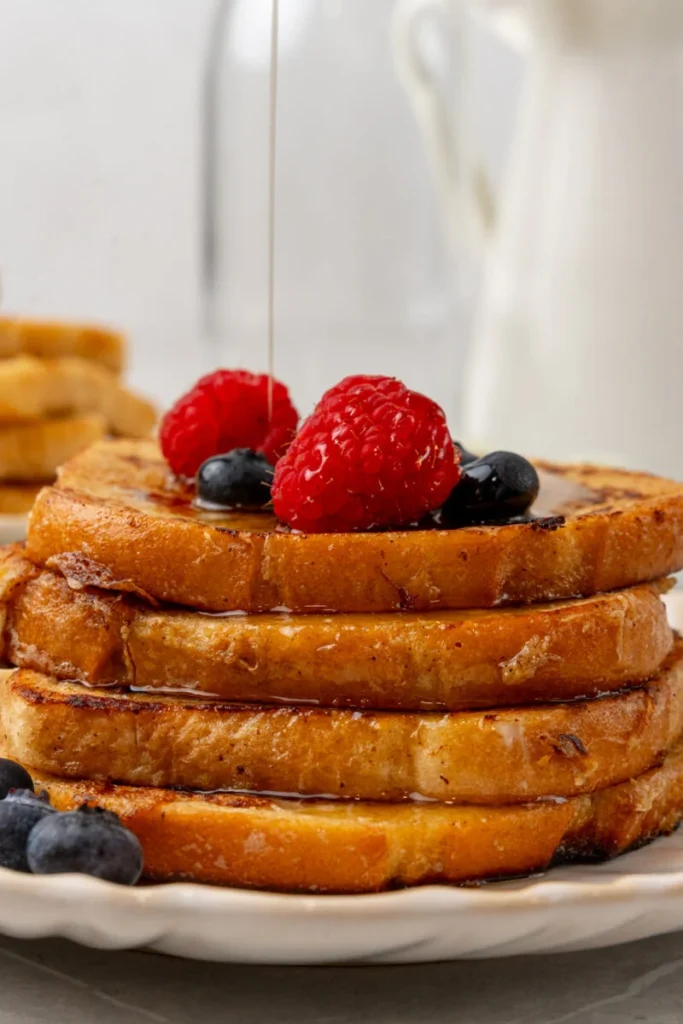 Stack of french toast slices drenched with syrup and fresh fruit.