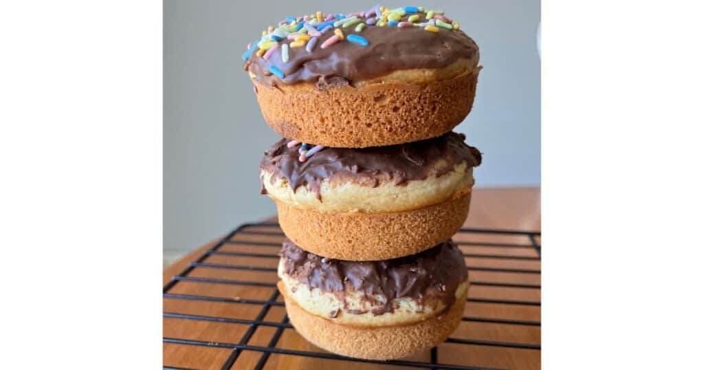 Stack of 3 vanilla cake donuts with chocolate glaze and colorful sprinkles.