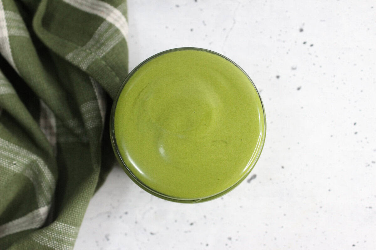 Matcha face cream in small jar next to a green plaid tea towel on countertop.