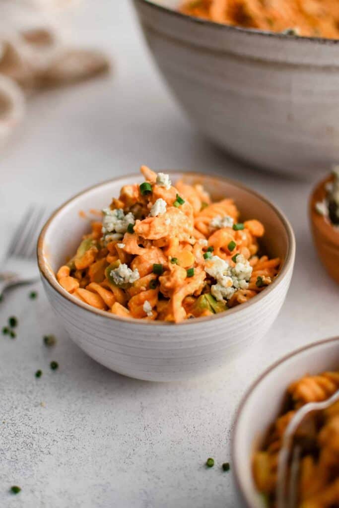 Buffalo chicken pasta topped with bleu cheese in a stoneware bowl.