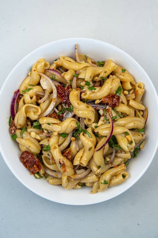 Fresh pasta salad with sun dried tomatoes in a white bowl.