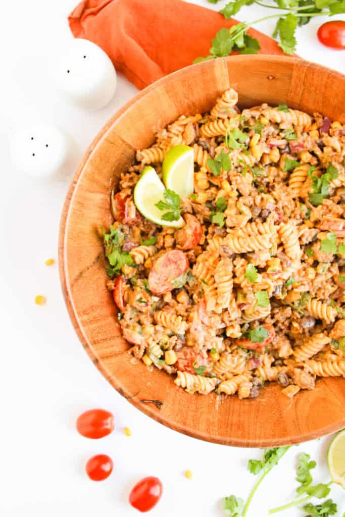 Pasta with taco seasoning and fresh herbs and lime in a large wooden bowl.