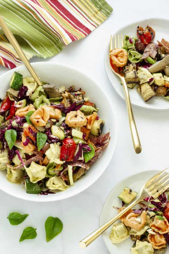 Pesto tortellini salad in a large bowl and on a lunch plate with a gold fork nearby.