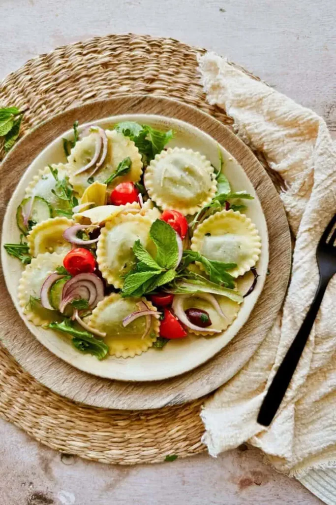 Bowl of tortellini pasta with vegetables in a wooden bowl on top of a rattan placemat.