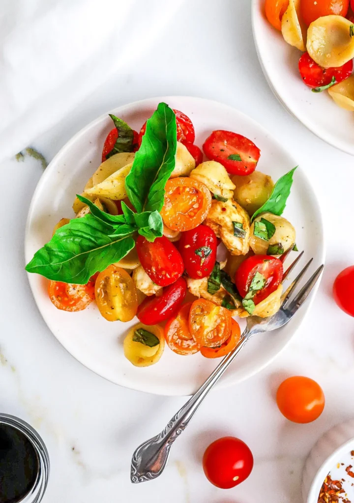 Salad with pasta, basil, cheese, tomato and dressing.