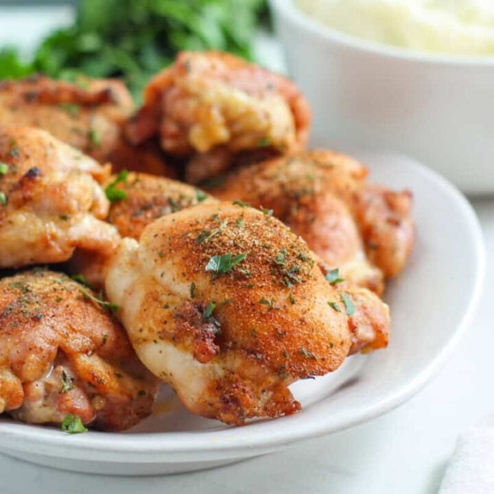 Oven roasted chicken thighs on white dish on white tabletop.