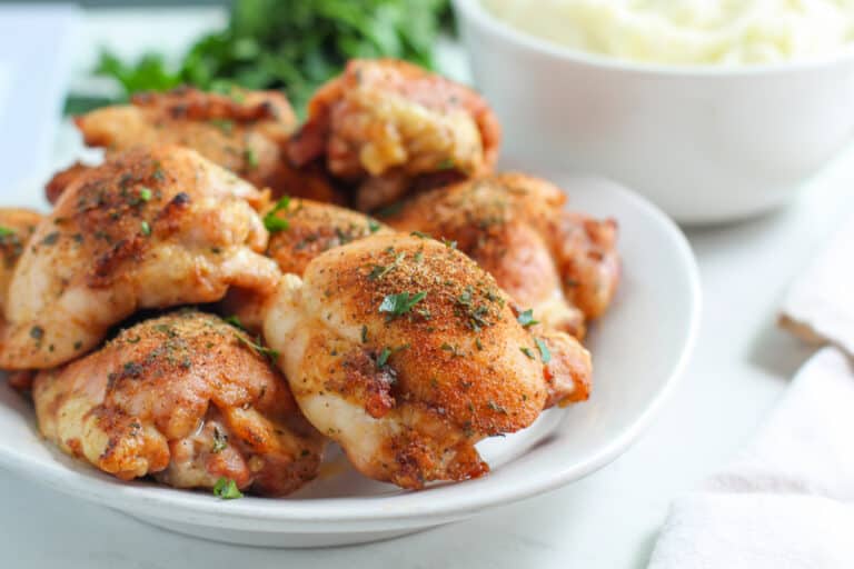 Oven roasted chicken thighs on white dish on white tabletop.