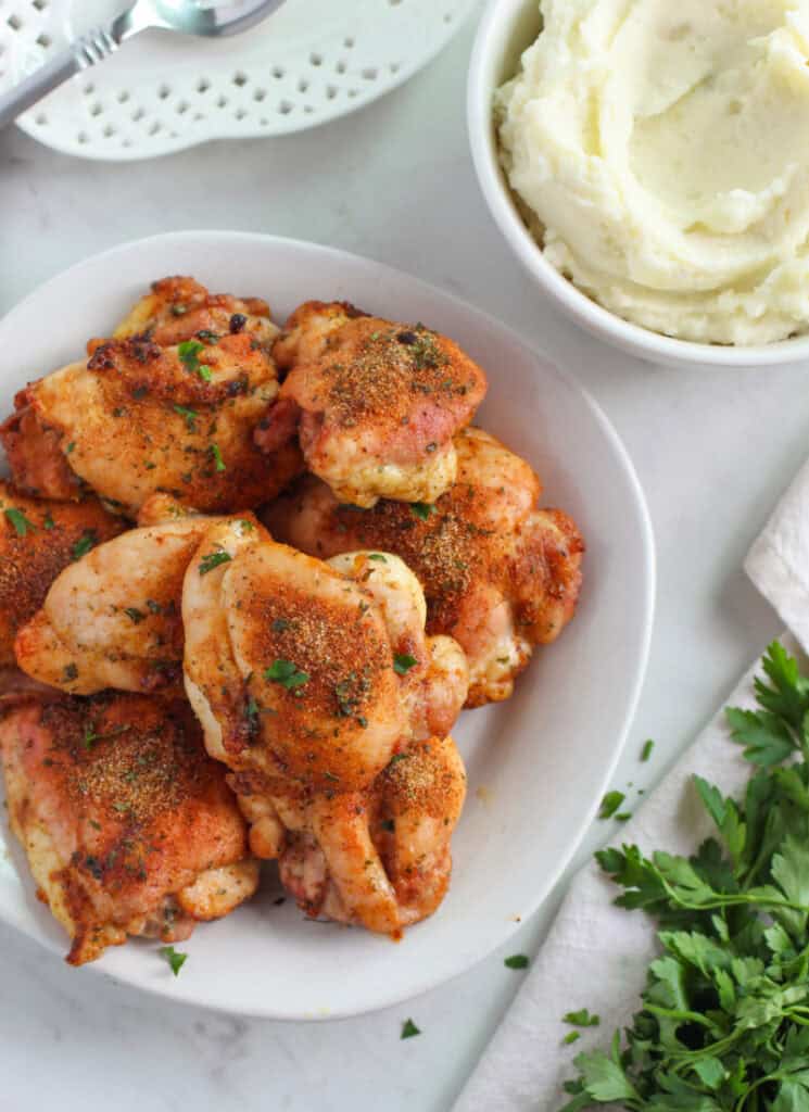 Roasted chicken thighs with mashed potatoes and parsley on table nearby for garnish.