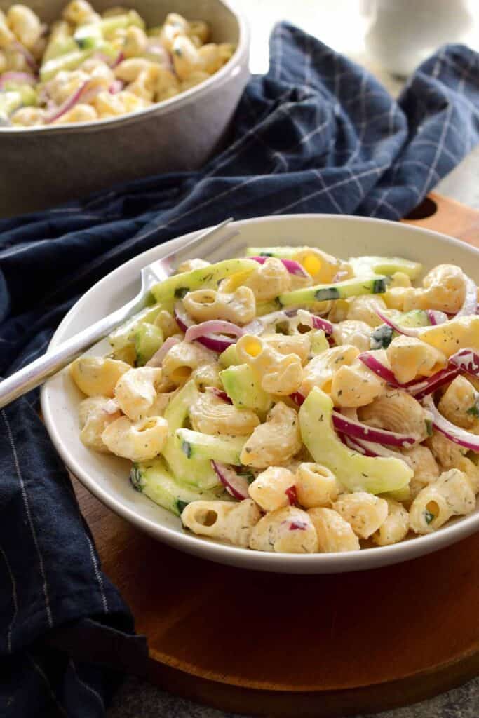 A creamy cucumber pasta salad in a shallow bowl with navy colored napkin nearby.