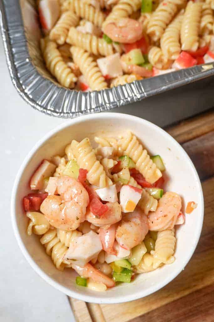Top view of a bowl of pasta with seafood and pan of seafood pasta in background.