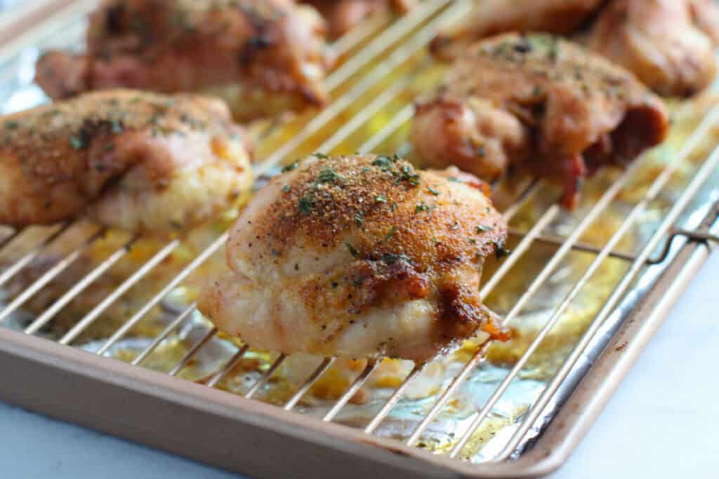 Chicken thighs baked and broiled on a wire rack over a sheet pan with crispy skin and seasoning on top.
