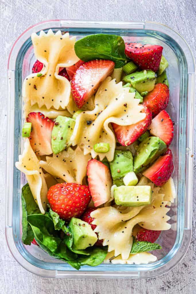 Clear container of strawberry, avocado and bowtie pasta salad.