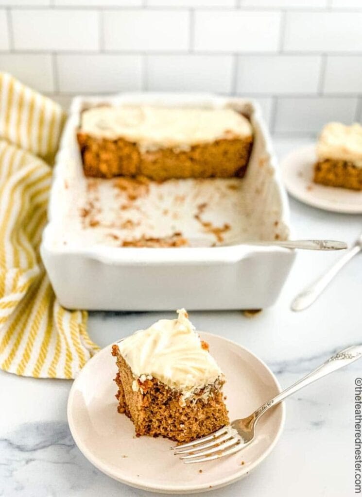 White dish of sourdough apple cake with piece of frosted cake on plate below.