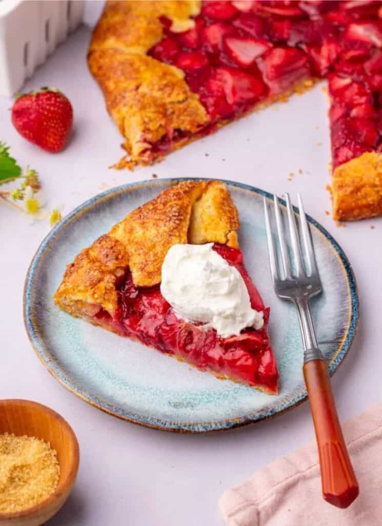 Slice of strawberry galette on a plate with full pie in background.