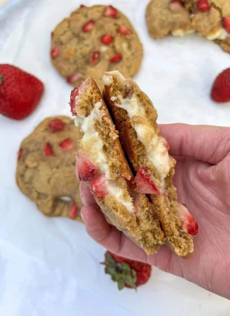 Hand holding a cookie split in half with cream cheese and strawberry filling.