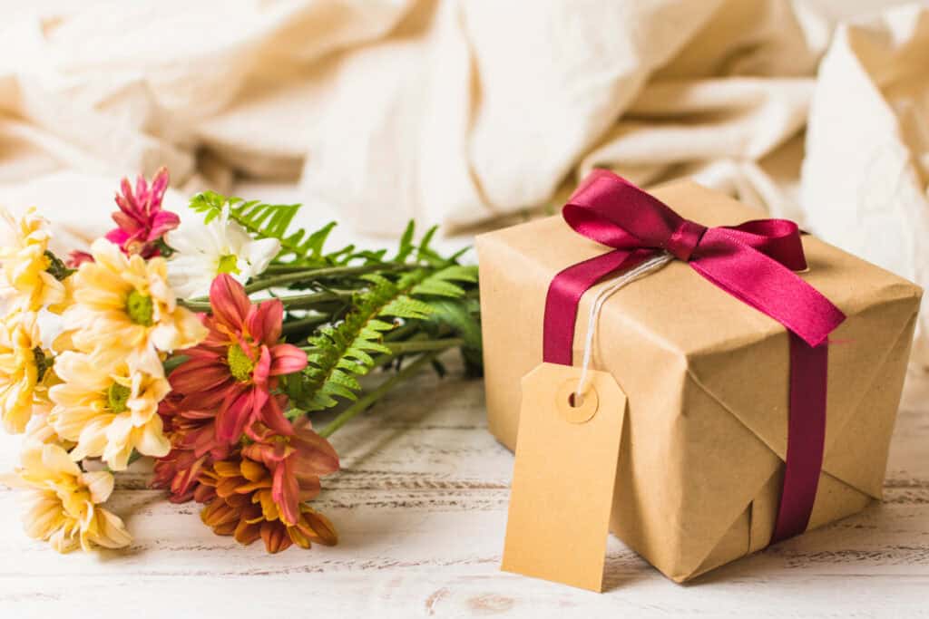 Handmade present wrapped in craft paper with bouquet of fresh flowers on table.