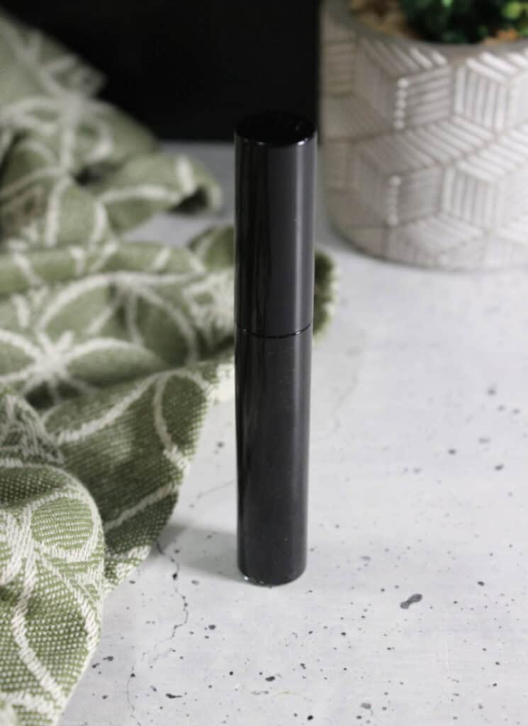 Mascara tube standing up on speckled white table top.