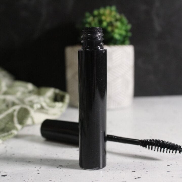 tube of mascara with wand on marble table top beside it and decorate plant nearby.