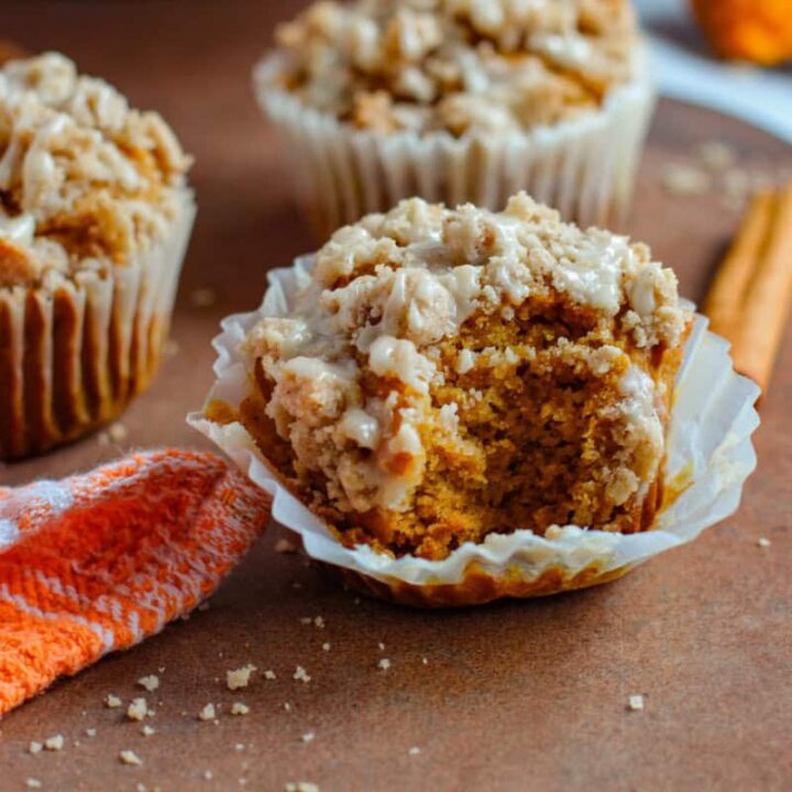 Pumpkin muffin with bite taken out of it and other muffins on table nearby.