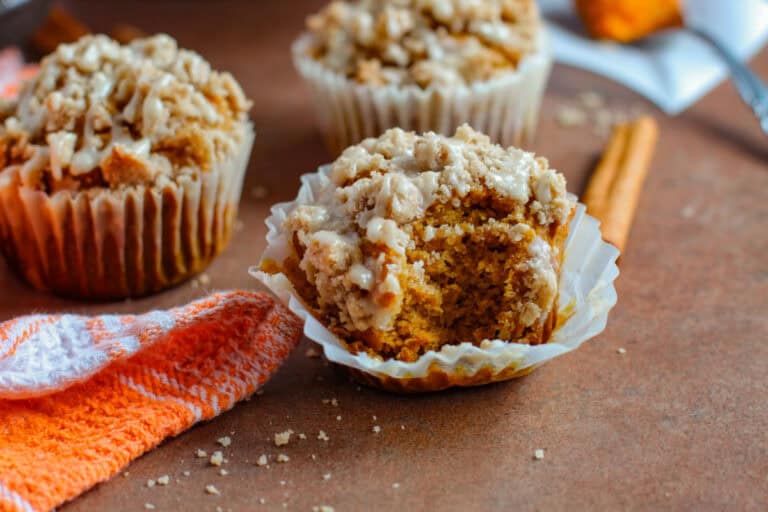 Pumpkin muffin with bite taken out of it and other muffins on table nearby.