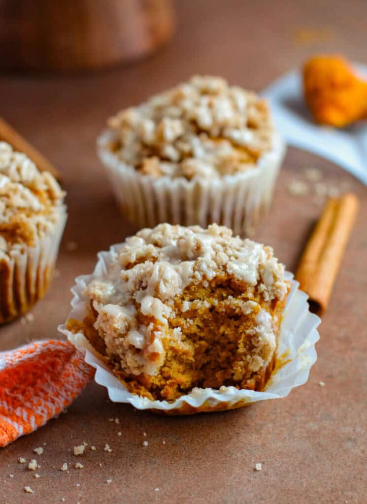 Pumpkin muffin on table with bite taken out of it and muffins in background.