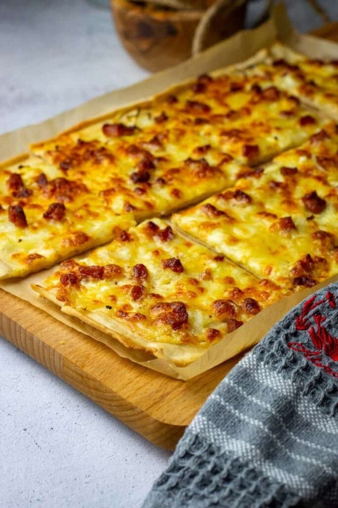 Sourdough flammkuchen with a thin crust sliced on a parchment sheet.