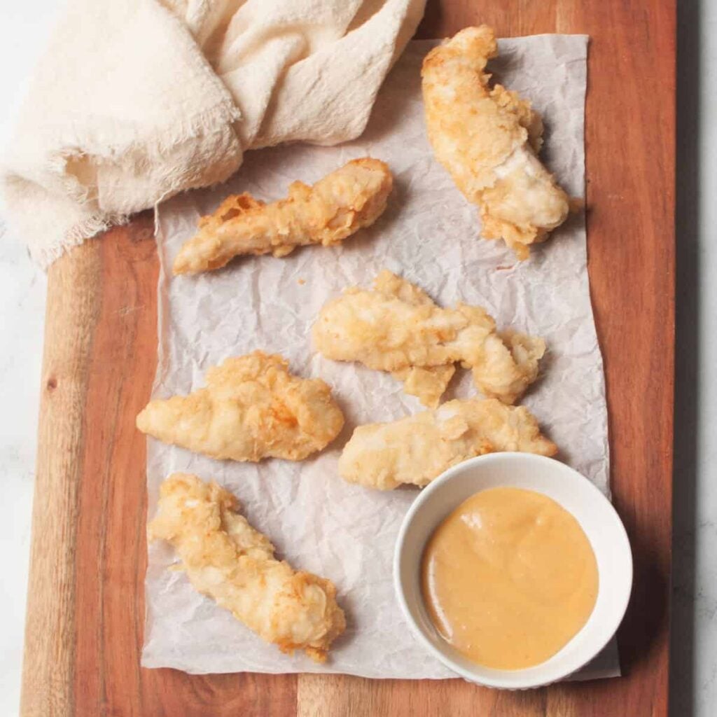 Breaded sourdough chicken tenders on parchment paper on a cutting board.