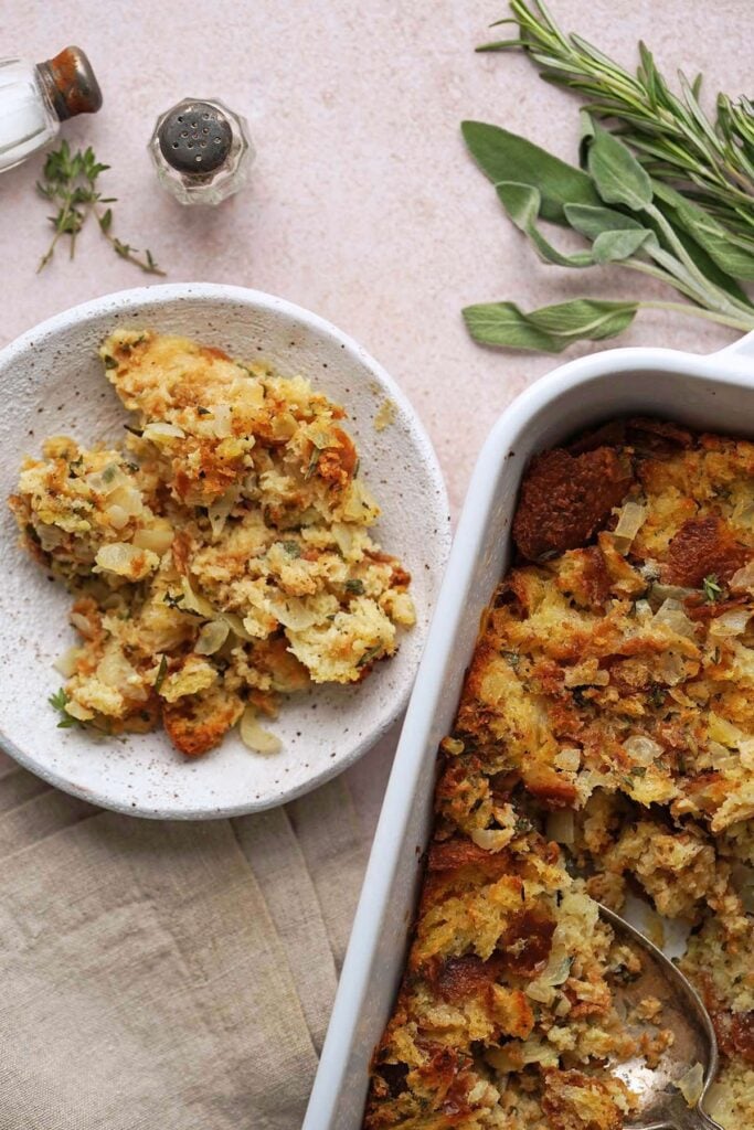 A bowl of stuffing with a baking dish of stuffing beside it on a rustic table.
