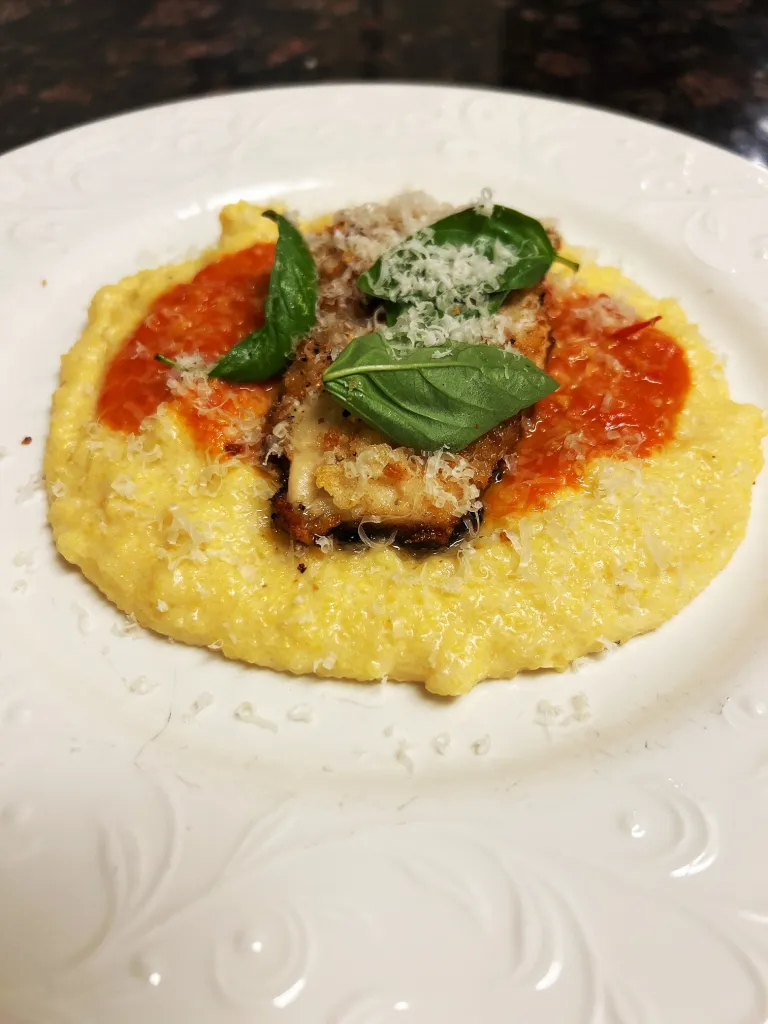 Chicken parmesan topped with basil on a bed of polenta.