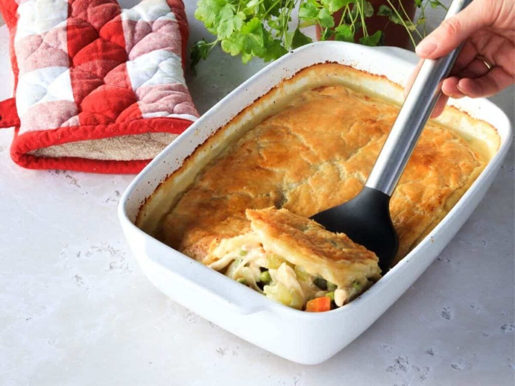 White baking dish with chicken pot pie and a spatula holding up a slice.