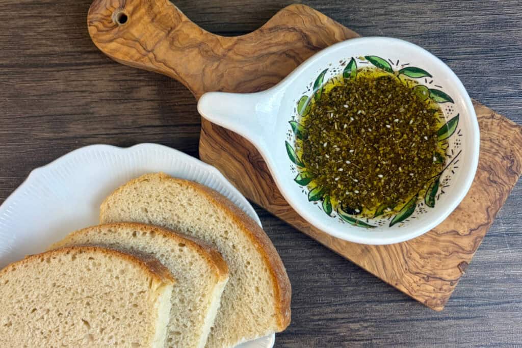 Olive dish with herbs and oil, and crusty bread nearby for dipping.