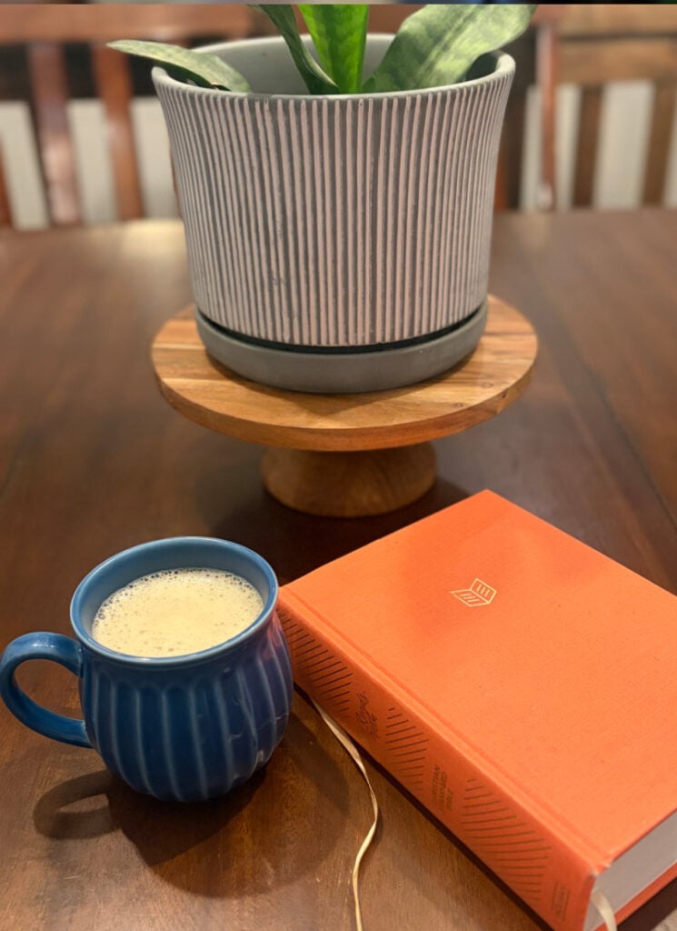 Cup of freshly brewed coffee with Bible and plant in background on kitchen table.